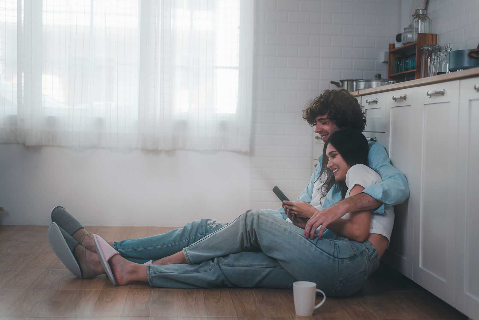 Image of a smiling couple sitting on the floor cuddling and looking at a cell phone. With EMDR therapy in Wake Forest, NC you and your partner can begin to work on your relationship in positive ways by overcoming past trauma.