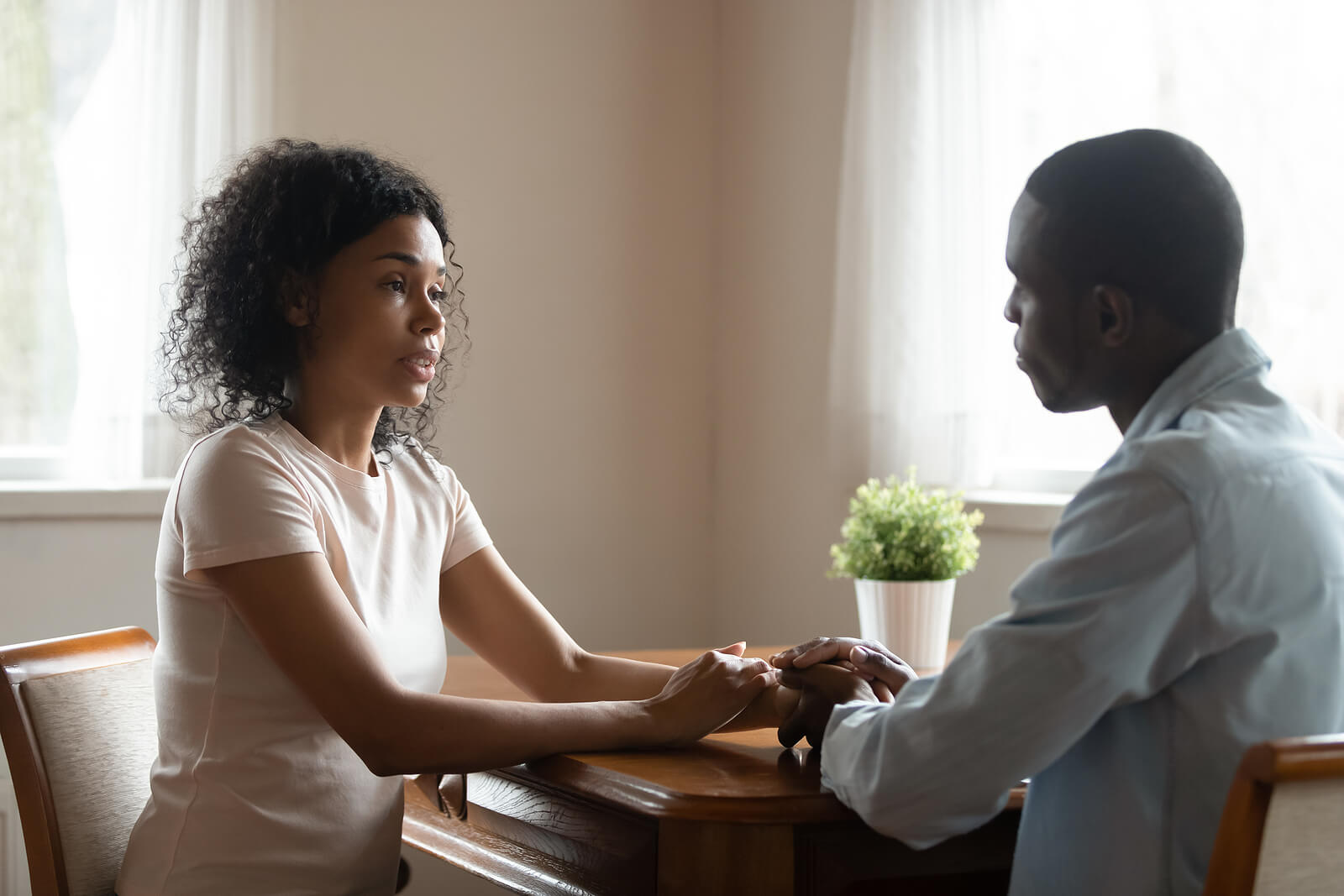 Image of a couple sitting at a table holding hands while having a serious conversation. With the support of EMDR therapy in Wake Forest, NC you and your partner can work to overcome personal trauma and strengthen your relationship.