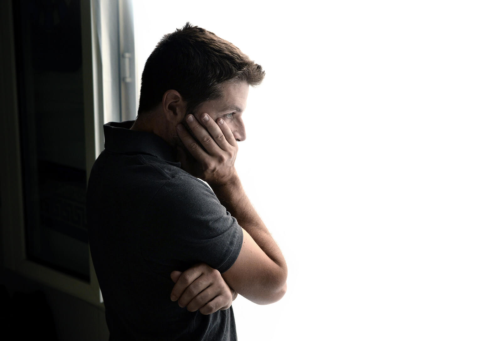 Image of a man resting a hand on his face looking out a window. Overcome unresolved trauma and begin healing to move forward with the support of EMDR therapy in Wake Forest, NC. 