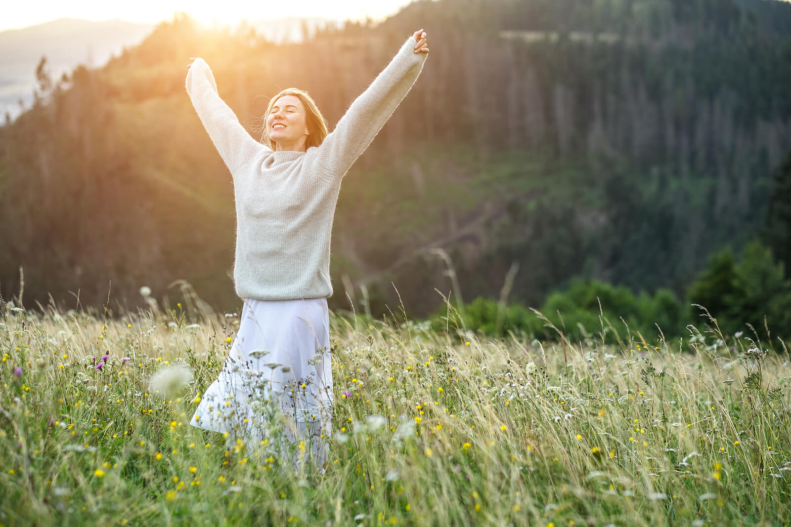 Image of a smiling woman standing in the middle of a field with her arms spread open. With the support of a skilled EMDR therapist in Wake Forest, NC you can begin working on your PTSD and unresolved trauma to start healing.