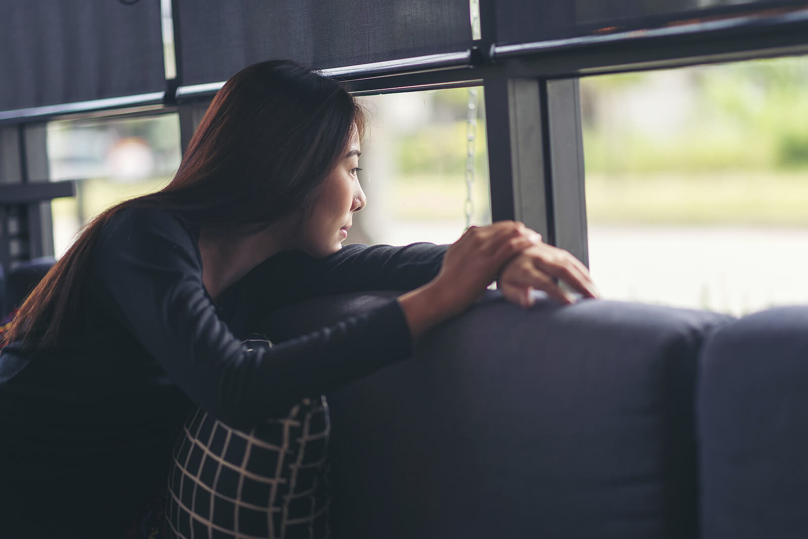 Image of a thoughtful woman sitting on a couch looking out a window. Discover how to cope and heal from your unresolved trauma with the help of EMDR Therapy in Wake Forest, NC.