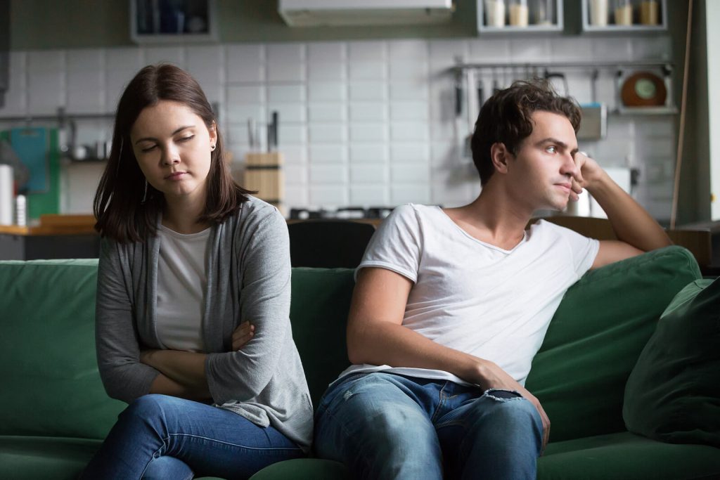 Image of a distant couple sitting on a couch facing away from each other. Begin strengthening the bond in your relationship with the support of EMDR therapy in Wake Forest, NC.