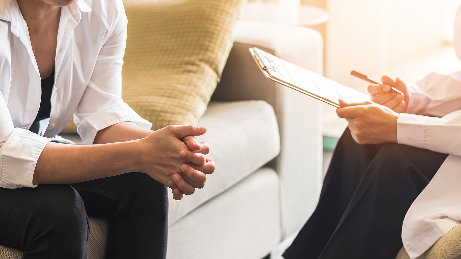 Image of a woman sitting on a couch leaning forward speaking with a therapist holding a clipboard. Discover how EMDR therapy in Raleigh, NC can help you effectively heal from distressing emotions.