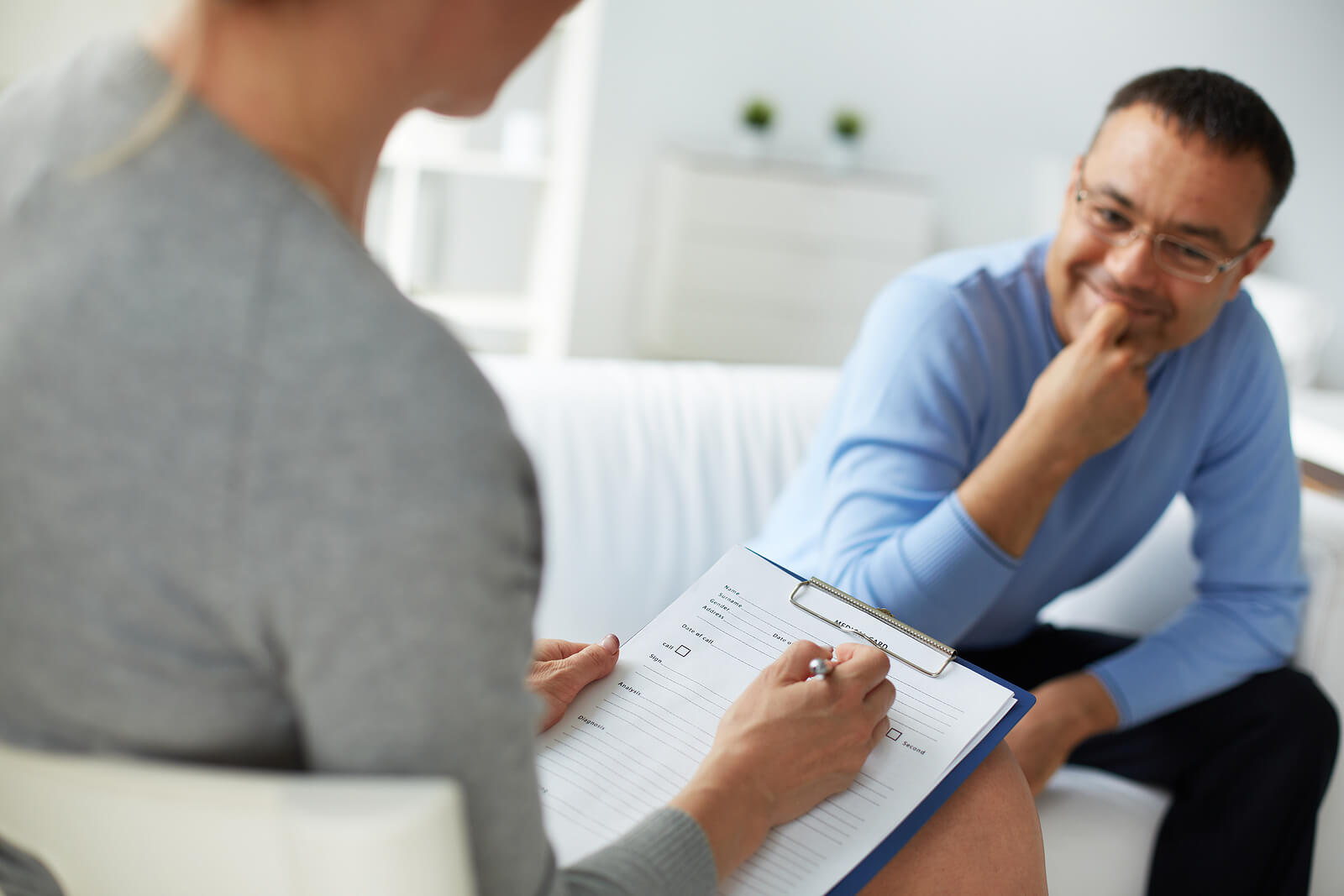 Image of a smiling man sitting on a couch speaking to a woman holding a clipboard. Overcome your anxiety, depression, or trauma with the support of a skilled EMDR therapist in Raleigh, NC.