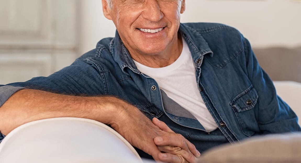 Image of a smiling relaxed older man sitting on a couch. Find support and relief from your trauma with the help of EMDR therapy in Raleigh, NC.