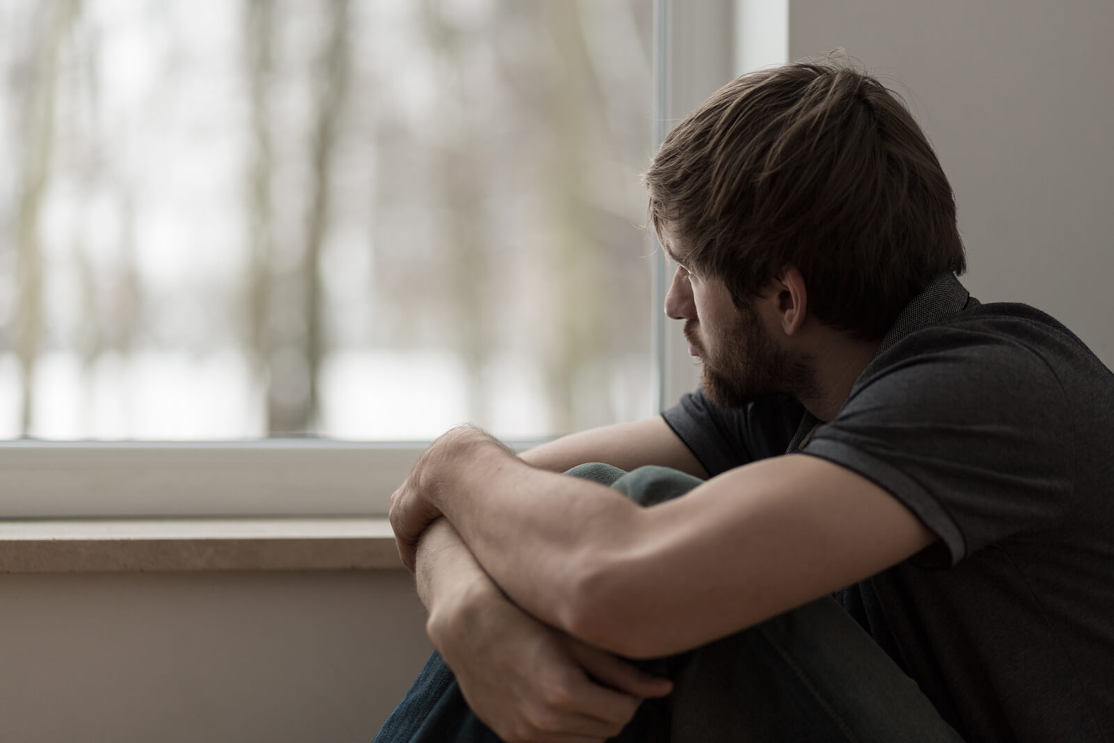 sad man looking out window | emdr therapy in raleigh, nc | emdr therapist in raleigh, nc | emdr therapy for childhood trauma | emdr trauma therapy | 27587 | 27608 | 27615 Image of a sad man resting his hands on his knees as he looks out a window. If you are struggling to overcome childhood trauma, find support healing with EMDR therapy in Raleigh, NC.