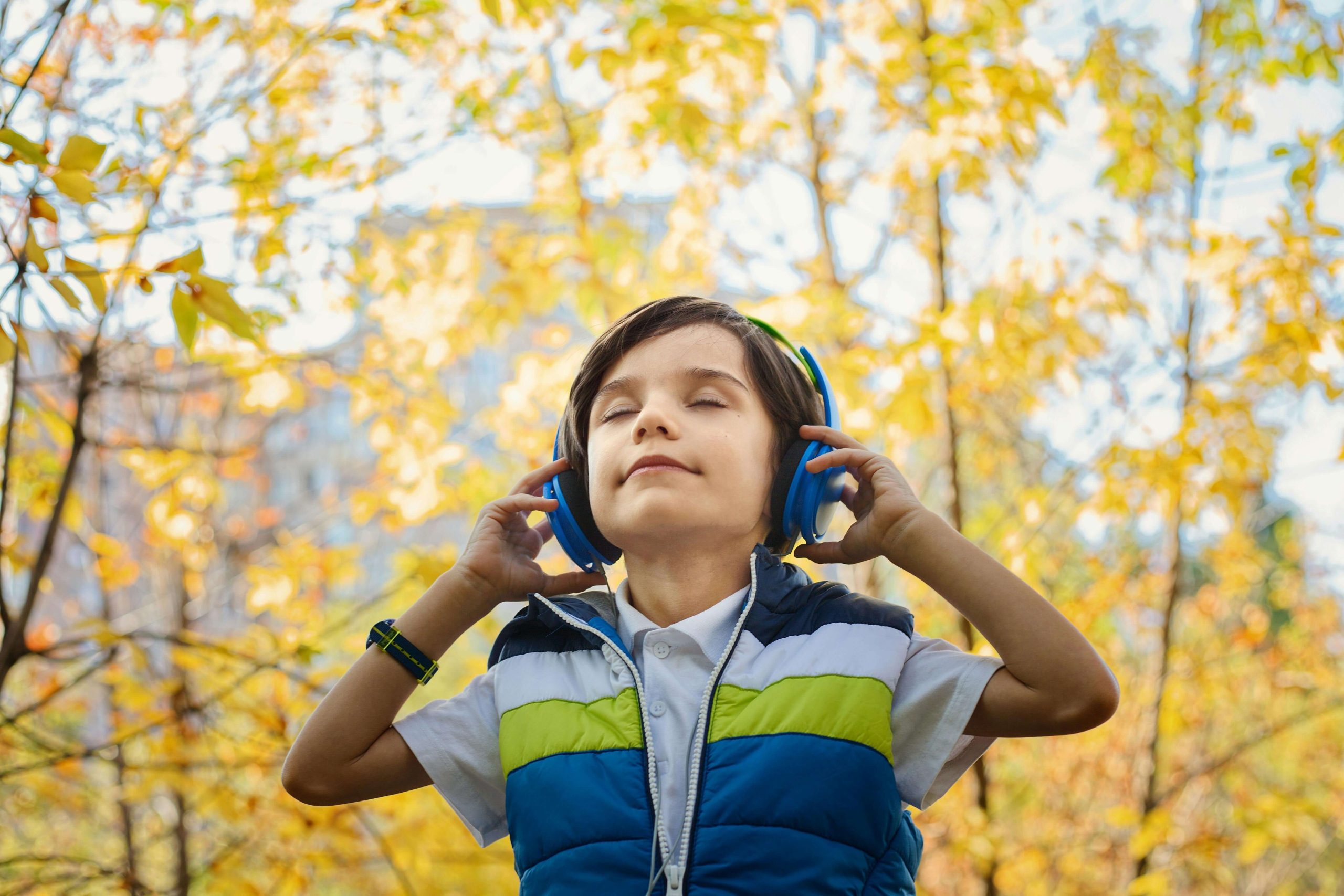 Image of a little boy standing in the forest with his eyes closed holding headphones against his ears. This image represents the peace your child can find after coping and healing from their anxiety symptoms with EMDR therapy in Raleigh, NC.