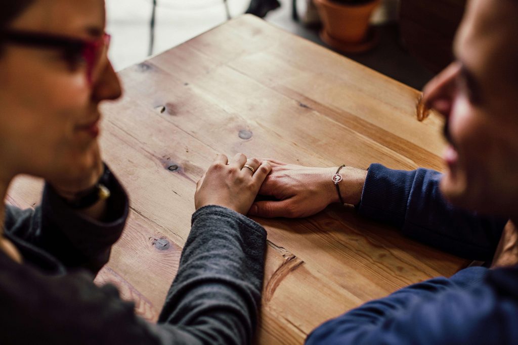 Image of a smiling couple sitting close at a table talking and holding hands. Learn to manage and cope with your emotional triggers due to trauma with the support of EMDR therapy in Raleigh, NC.