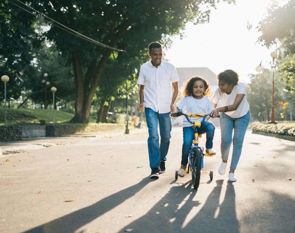 Happy family walking down street helping young girl ride a bicycle. Begin supporting your child and help them cope with their anxiety with the help of EMDR therapy for children in Raleigh, NC.