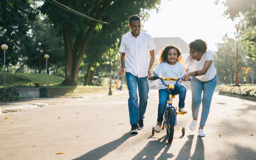 Happy family walking down street helping young girl ride a bicycle. Begin supporting your child and help them cope with their anxiety with the help of EMDR therapy for children in Raleigh, NC.