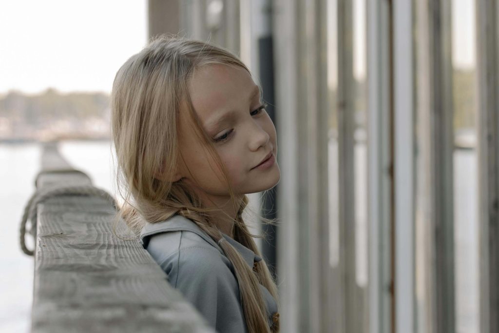 Thoughtful young blonde girl leaning on a railing. See your child begin to thrive and heal after struggling with trauma with EMDR therapy in Raleigh, NC.
