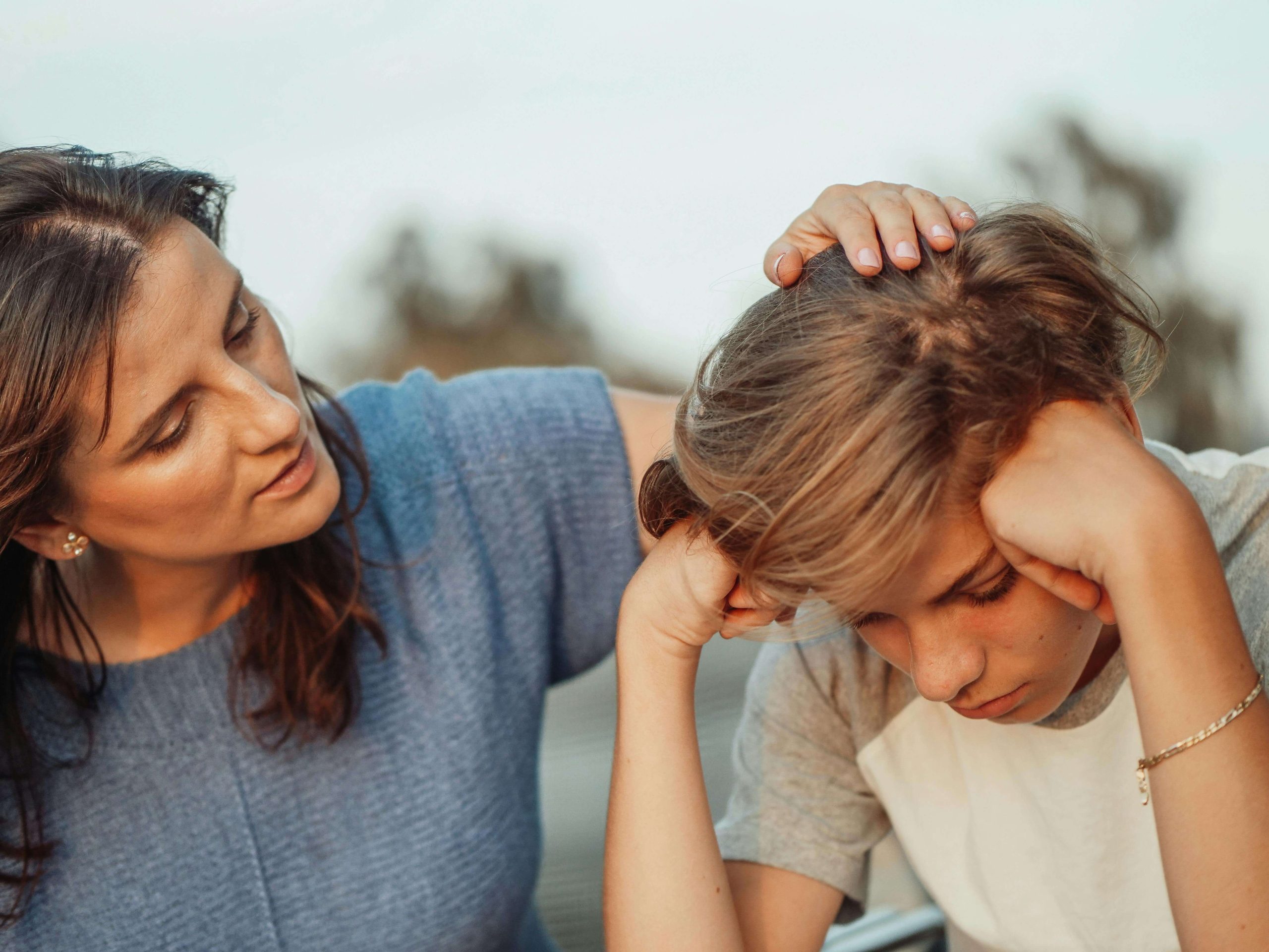 Mother touching her upset son's head trying to comfort him. If your child is struggling with unseen trauma, give them the support they need to heal with the help of an EMDR therapist in Raleigh, NC.