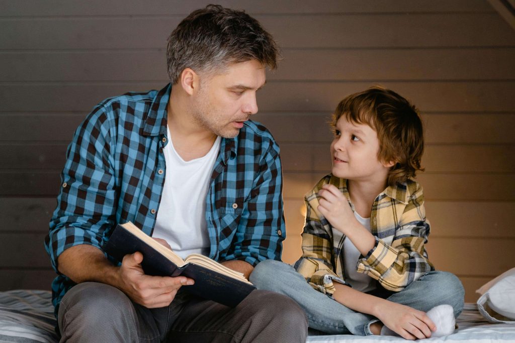 Happy man and little boy sitting next to each other reading a book. Begin to heal from your childhood trauma and begin coping in positive ways with EMDR therapy in Raleigh, NC.