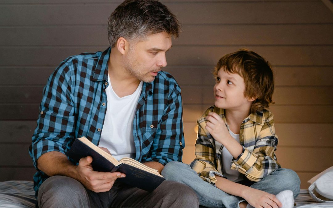 Happy man and little boy sitting next to each other reading a book. Begin to heal from your childhood trauma and begin coping in positive ways with EMDR therapy in Raleigh, NC.
