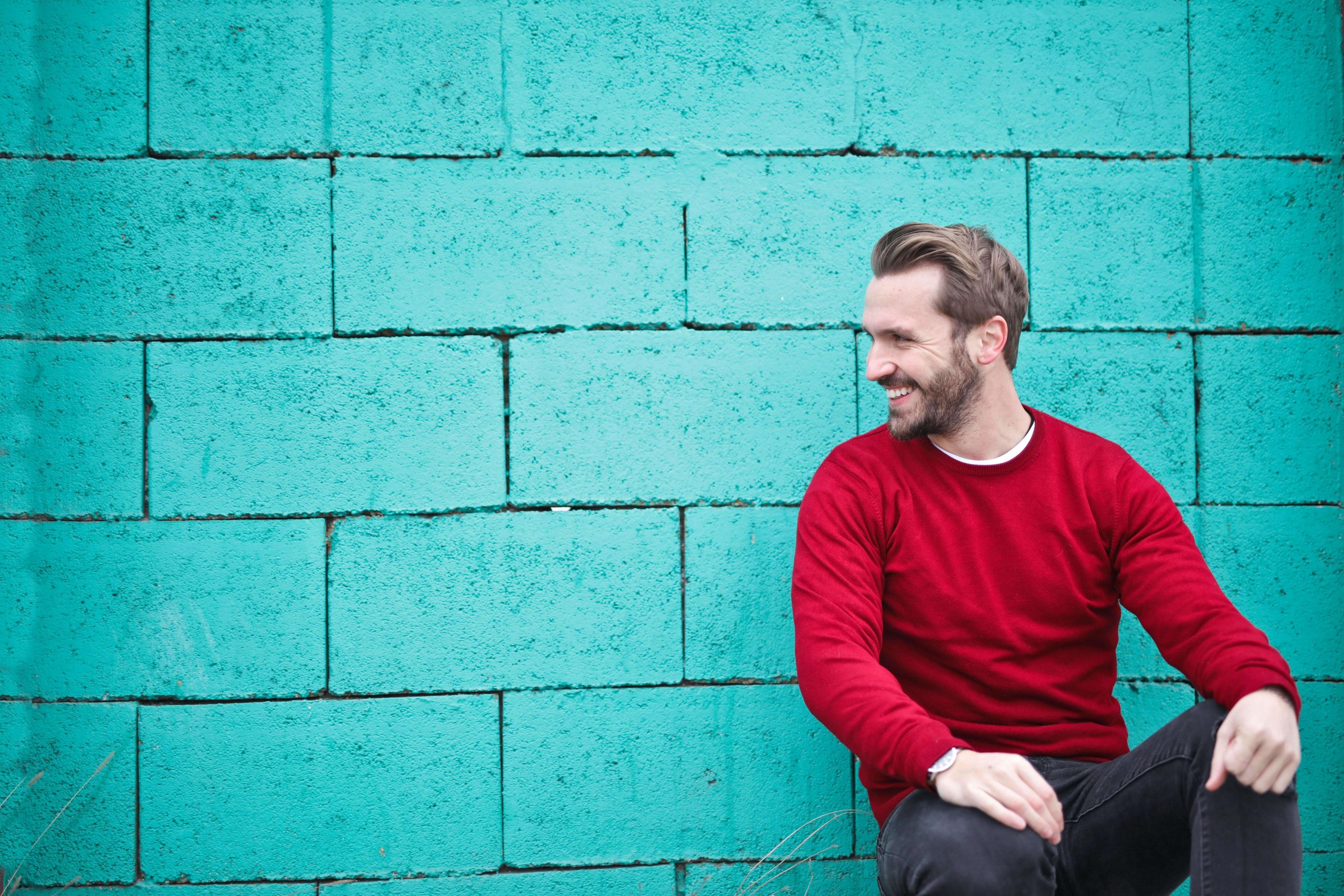 happy man | emdr therapy in raleigh, nc | emdr therapist | emdr trauma therapy | emdr for couples | Five Points | Boylan Heights | Wakefield Happy man sitting on the ground next to a teal wall. Break free from the emotions holding you back after a breakup with the help of EMDR therapy in Raleigh, NC.