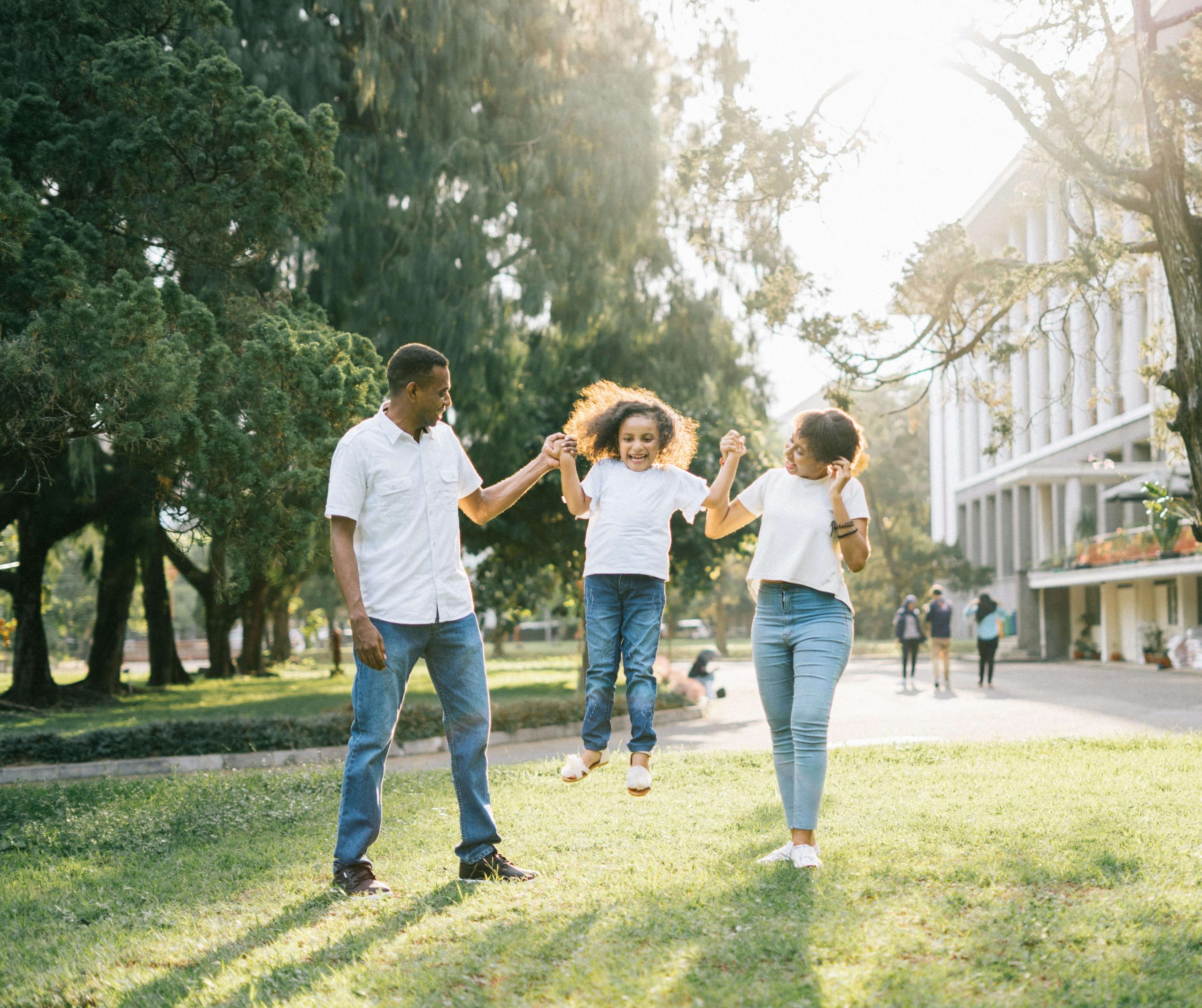 Happy parents lifting up their smiling young daughter on a sunny day in the park. See positive changes in your child after they've been struggling with trauma with the support of a compassionate EMDR therapist in Raleigh, NC.