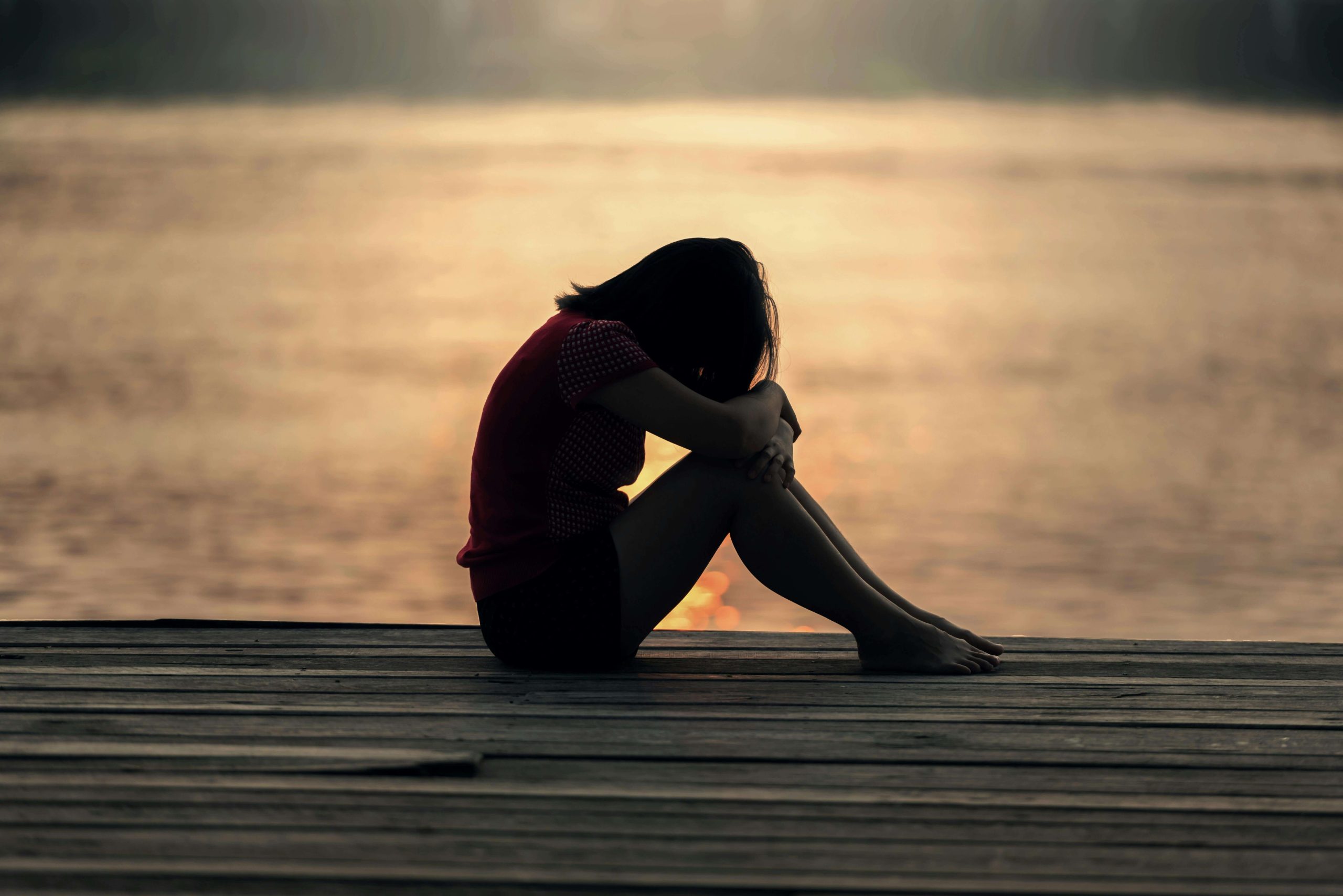 sad girl | emdr therapy in raleigh, nc | emdr therapist | emdr for childhood trauma | emdr childhood trauma | Five Points | Boylan Heights | Brier Creek | Wakefield Sad little girl sitting at the end of a pier with her head in her lap. With the support of EMDR therapy for childhood trauma in Raleigh, NC you can begin to heal in healthy ways and prevent generational trauma.